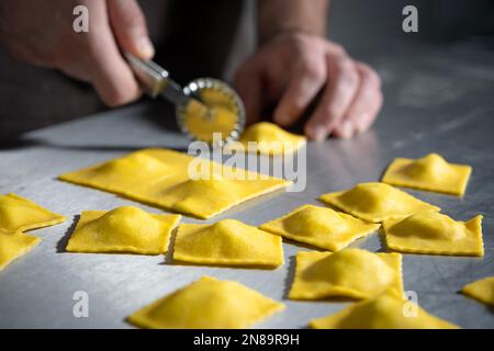 Jeune homme Chef de la fabrication des raviolis. Plats italiens raviolis de pâtes maison sur fond métallique. Banque D'Images