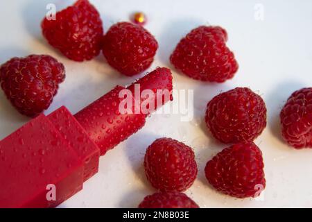 Rouge à lèvres brillant et framboises mûres juteuses sur fond blanc. Banque D'Images