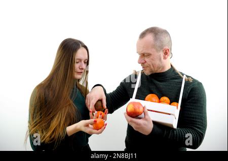 Boutique de fruits homme adulte de panier blanc sous forme de boîte en bois vend différents fruits mandarines pomme kiwi persimmon jeune fille cheveux longs sur fond blanc magasin de publicité produits savoureux Banque D'Images