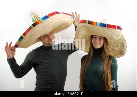 homme adulte et jeune fille tiennent sur leur tête sombrero chapeau espagnol headors joie acheter à la fois dans vert foncé golfs sur la marche headaddress vente vêtements joyeux voyage vacances mexicaines buenos muchachos Banque D'Images