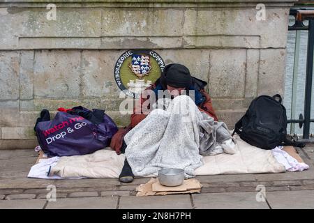 Windsor, Berkshire, Royaume-Uni. 11th février 2023. Un homme sans abri dort sur le pont de Windsor avec un bol de dons. Crédit : Maureen McLean/Alay Live News Banque D'Images