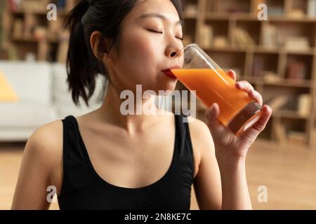 Détox régime et perte de poids. Jeune femme asiatique buvant du jus, déjeuner après l'entraînement domestique, gros plan Banque D'Images