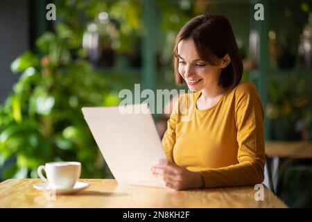 Jolie jeune femme qui se rafraîchlait au café, qui boit du café, qui lit le menu Banque D'Images