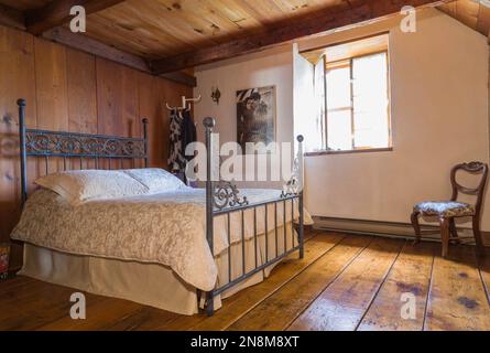 Lit double avec tête de lit et pied de lit en fer forgé antique, fauteuil rembourré à motifs floraux dans la chambre principale à l'étage à l'intérieur de la vieille maison. Banque D'Images