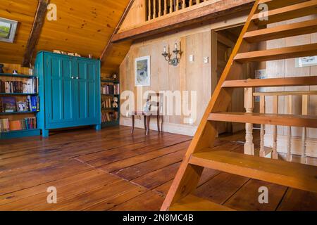 Armoire en bois antique peinte en bleu sarcelle, bibliothèque, chaise rembourrée rouge et escalier de Pinewood Miller dans la salle de lecture à l'étage à l'intérieur de la vieille maison de 1760. Banque D'Images