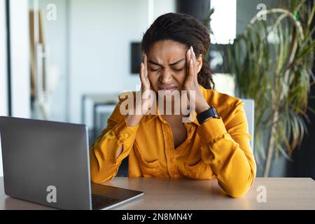 Triste femme d'affaires assise avec un ordinateur portable sur le lieu de travail, souffrant de maux de tête, touchant des temples, travaillant au bureau Banque D'Images