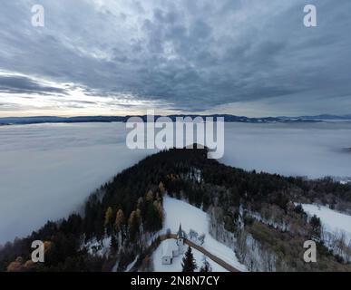 Une photo aérienne de l'église de Saint Primus et Felician au sommet d'une montagne forestière enneigée, Slovénie Banque D'Images