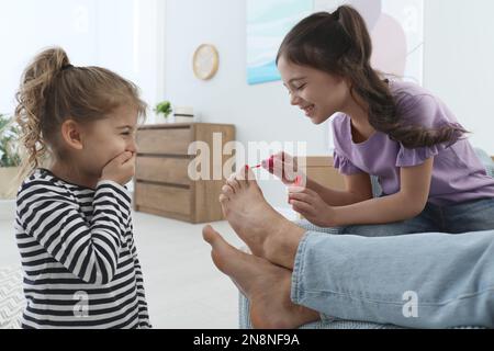 Petits enfants mignons appliquant du vernis sur les ongles du père pendant qu'il dormait à la maison, en gros plan Banque D'Images