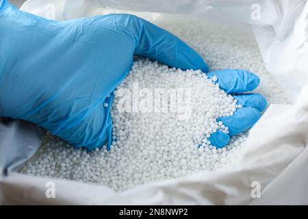 Personne en gants prenant des pastilles de nitrate d'ammonium dans le sac, gros plan. Engrais minéral Banque D'Images