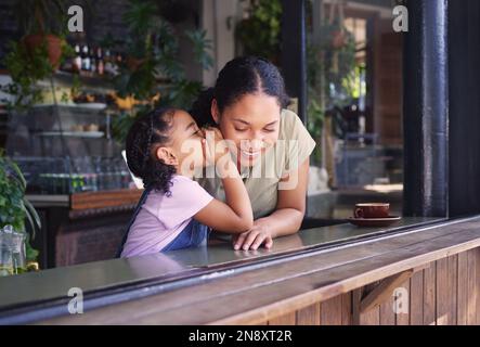 Secret, des enfants et une famille noire dans un café avec une fille chuchotant à l'oreille de sa mère. Enfants, potins et murmures avec une femelle secrète Banque D'Images