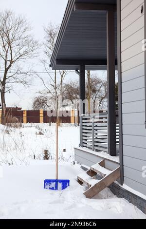 Cour couverte de neige près de la maison avec une pelle coincée dans la neige, déneigement de la région Banque D'Images