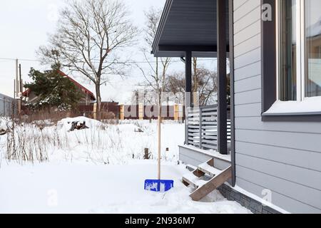 Cour enneigée près de la maison avec une pelle coincée dans la neige, déneigement du site Banque D'Images
