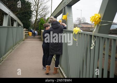 NOTE DE LA RÉDACTION: LA PERMISSION PARENTALE ACCORDÉE À Une femme et un jeune garçon d'attacher un ruban jaune avec un message d'espoir écrit dessus, à un pont au-dessus de la rivière Wyre à St Michael's sur Wyre, Lancashire, alors que la police continue leur recherche pour la femme disparue Nicola Bulley, 45, Qui a été vu pour la dernière fois le matin de vendredi 27 janvier, quand elle a été repérée marchant son chien sur un sentier de randonnée près de la rivière Wyre. Date de la photo: Dimanche 12 février 2023. Banque D'Images