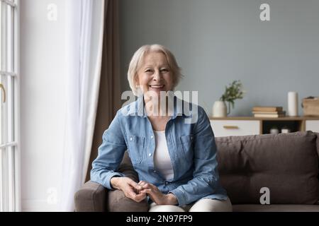 Joyeuse positive dame senior assise sur un canapé, souriante, riant Banque D'Images