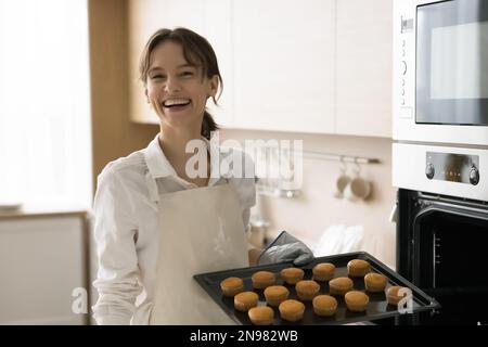 Joyeuse jolie jeune femme boulangère en tablier pour cuire des petits gâteaux faits maison Banque D'Images