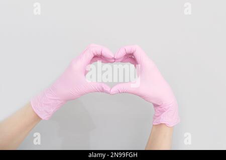 Mains du médecin en gants médicaux roses en forme de coeur sur fond gris, espace de copie. santé, pharmacie et médecine, soins pour la santé cardiaque. Banque D'Images