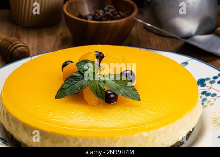 Vue rapprochée de délicieux cheesecake à la pêche maison garni de morceaux de pêche conservés, de myrtille et de feuilles de menthe verte dans un plat en céramique blanche Banque D'Images