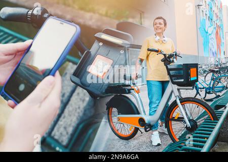 Femme prend un vélo loué dans un parking à vélos avec un smartphone Banque D'Images