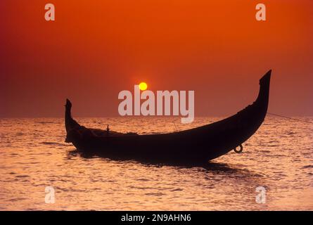Le soleil cadre encadré par la poupe en forme de croissant d'un catamaran à Kozhikode, Calicut, Kerala, Inde Banque D'Images