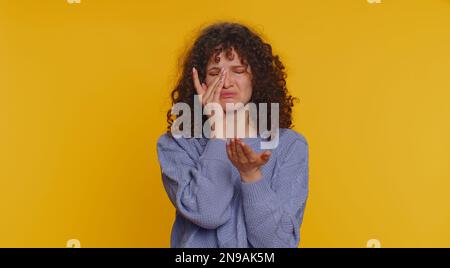 Bouleversée, déçue, jeune femme aux cheveux mauriques essuie des larmes et des cris de désespoir, étant triste en raison de choses injustes. Jeune fille dans la dépression, le désespoir, la perte isolée seule sur fond jaune studio Banque D'Images