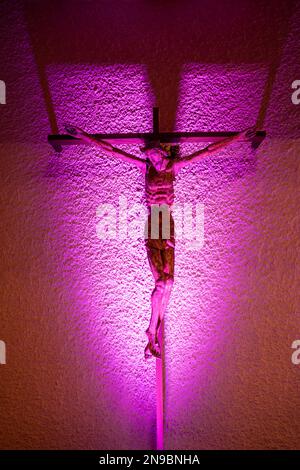 Hunenberg, Suisse - 9 décembre 2022 : le crucifix sur le mur de l'église, illuminé par la lumière pourpre Banque D'Images