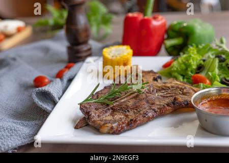 Steak de bœuf avec salade de légumes servi sur une assiette blanche sur une table en bois Banque D'Images