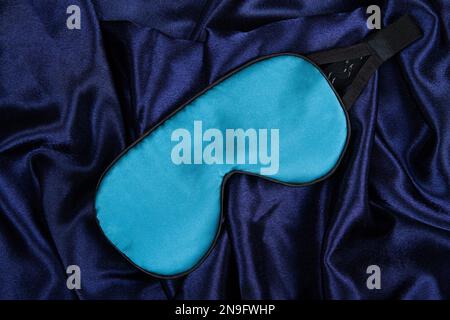 Le masque de sommeil en soie bleu clair repose sur un fond bleu foncé soyeux Banque D'Images