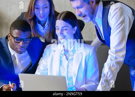 4 personnes d'une équipe diversifiée ont une discussion autour d'un ordinateur portable dans la journée dans un espace ouvert. Ils sont énergiques et joyeux comme ils smil Banque D'Images