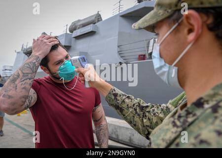 La température d’un marin affecté au destroyer à missiles guidés USS Kidd (DDG 100) est vérifiée lorsqu’il retourne au navire dans le cadre de la réaction agressive de la Marine à l’épidémie de COVID-19. Banque D'Images