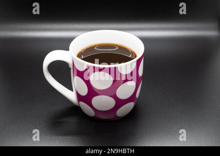 Tasse à café rose avec cercles blancs isolés sur fond noir Banque D'Images