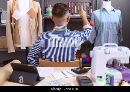 Homme hispanique avec couturier de barbe designer travaillant à l'atelier posant en arrière pointant vers l'avant avec le doigt de la main Banque D'Images