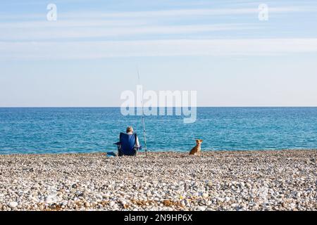 un pêcheur et un chien sont assis sur la mer Banque D'Images