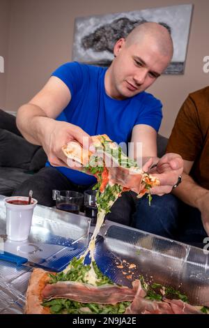 Deux amis qui mangent de la pizza. S'amuser et faire la fête à la maison. Banque D'Images