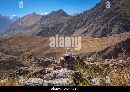 Une jeune fille touristique s'assoit sur une pierre dans les montagnes et regarde la carte de l'itinéraire pour un voyage plus long Banque D'Images