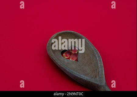 Cuillère en bois avec un trou en forme de coeur rempli de pilules d'huile de poisson isolées sur fond rouge. Concept de la cuisine et de la santé Banque D'Images