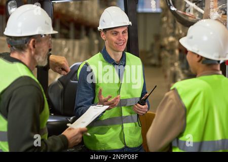 Portrait de jeune homme souriant qui parle à un groupe de travailleurs dans l'entrepôt Banque D'Images