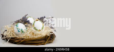 pâques bannière vue latérale des oeufs dans le nid lavande fleurs ruban broderie sur coquille blanc oeufs sont sur la paille sur l'espace droit pour le texte publicité carte postale panneau d'affichage vacances de pâques Banque D'Images