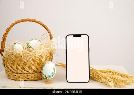 Téléphone de vacances de Pâques avec fond blanc espace vide pour la publicité dans le panier œufs avec motif brodé ruban brodé sur les épillets de blé de coquille d'œuf sur la table place pour la pâte gros plan panier Banque D'Images