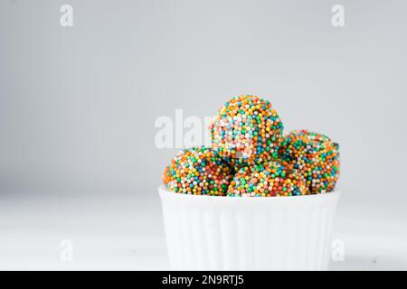 saupoudrer les truffes enrobées de chocolat dans un ramequin blanc, les bonbons au chocolat faits maison couverts de fruits non paréels sur fond blanc Banque D'Images