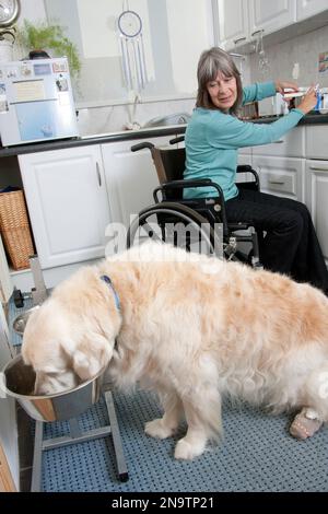 Femme handicapée en fauteuil roulant dans une cuisine avec son chien Banque D'Images