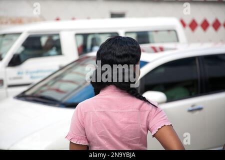 Jeune femme aux cheveux longs qui regarde les véhicules dans la rue ; Bridgetown, Barbade Banque D'Images