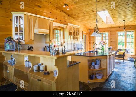 Buffet en bois d'érable, îlot avec comptoir en granit poli et placards dans la cuisine avec plancher en ardoise à l'intérieur pièce sur pièce maison en rondins. Banque D'Images