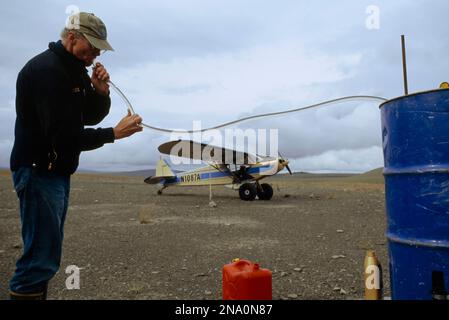 Un pilote de petit avion siphonne le gaz d'un char ; North Slope, Alaska, États-Unis d'Amérique Banque D'Images