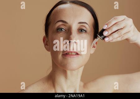 femme moderne de 40 ans avec élixir cosmétique isolée sur beige. Banque D'Images