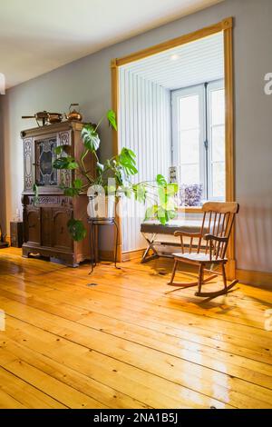 Chaise à bascule en bois antique, plante verte et buffet dans le salon avec parquet en pin à l'intérieur de la vieille maison de 1820. Banque D'Images