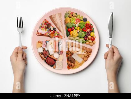 Femme tenant des couverts près de l'assiette avec différents produits sur fond blanc, vue de dessus. Nourriture équilibrée Banque D'Images