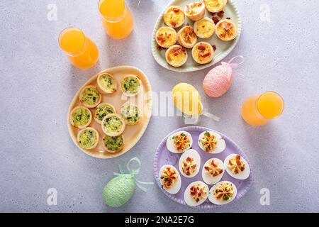 Œufs dévorés et mini quiches, hors-d'œuvre pour le brunch de Pâques avec cocktails mimosa Banque D'Images