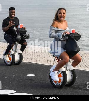 Un couple qui suit un chemin sur Segways au bord de l'eau et souriant pour la caméra; Lisbonne, quartier de Setubal, Portugal Banque D'Images