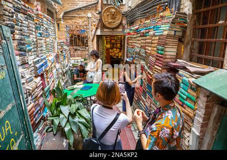 Un touriste photographie une femme choisissant un livre parmi les piles de livres dans un magasin ; Venise, Italie Banque D'Images