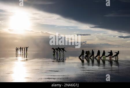 Touristes posant dans le reflet pendant la saison humide (décembre-février) dans le Salar de Uyuni, la plus grande plate-forme saline du monde Banque D'Images